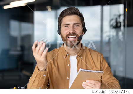 Business professional in virtual video call demonstrating communication skills. Engaging expression, wearing headset, holding notebook. Ideal for concepts of remote work, virtual meetings, technology Business professional in virtual video call demonstrating communication skills. Engaging expression, wearing headset, holding notebook. Ideal for concepts of remote work, virtual meetings, technology 127837372
