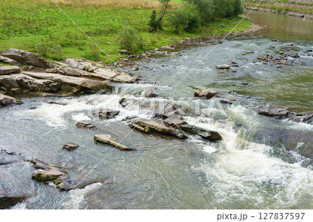 Closeup of powerful waterfall, fast river rushing over mossy rocks in mountain stream scenery Closeup of powerful waterfall, fast river rushing over mossy rocks in mountain stream scenery 127837597