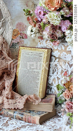 A book is on top of a stack of books and a lace tablecloth 127838084