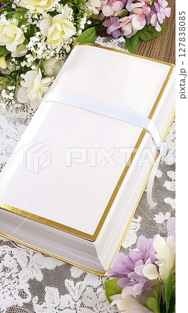 A white book with gold trim sits on a table with flowers 127838085
