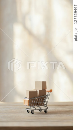 Small cardboard boxes inside a miniature shopping cart sit on a wooden table, representing online shopping, e commerce, and delivery concepts with a bright background 127839467