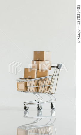 Miniature shopping cart carrying cardboard boxes suggesting the concept of online shopping, delivery and e commerce, with a neutral background and reflection 127839483