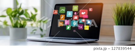 Open laptop displaying colorful application icons floating above the screen, representing social media marketing and application development in a bright office environment 127839544