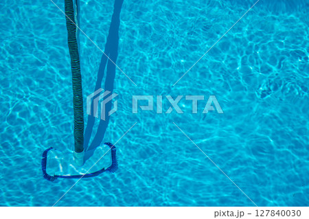 Manual pool vacuum with flexible hose and telescopic pole cleaning the bottom of a clear swimming pool during regular maintenance in bright sunlight. Manual pool vacuum with flexible hose and telescopic pole cleaning the bottom of a clear swimming pool during regular maintenance in bright sunlight. 127840030