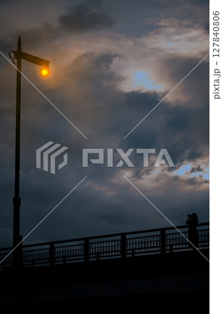 橋の上にある街灯のシルエットと夕焼け 127840806