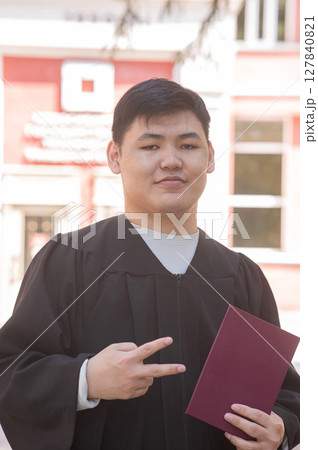 Asian young man in graduation gown holding diploma.  127840821