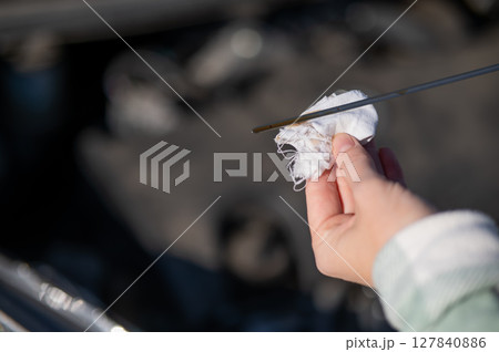 Close up of hands of female driver checking oil level in car engine. Close up of hands of female driver checking oil level in car engine. 127840886