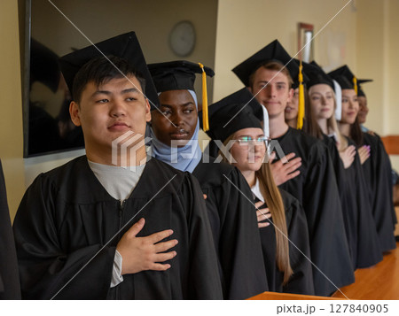 Graduates stand proudly at the ceremony with their hands over their hearts.  127840905
