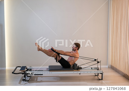A man doing Pilates on a reformer.  127841068