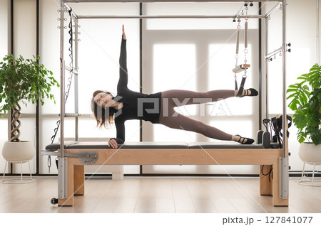 Woman doing Pilates on reformer. Woman doing Pilates on reformer. 127841077