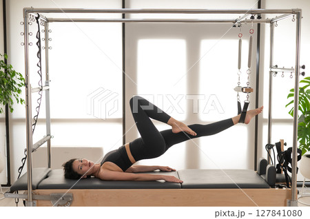 Asian woman doing pilates on reformer.  127841080
