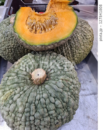 At a bustling farmers market in Marina di Chioggia, Spain, vibrant green and orange pumpkins are displayed. The pumpkins highlight local agriculture, attracting visitors and shoppers. At a bustling farmers market in Marina di Chioggia, Spain, vibrant green and orange pumpkins are displayed. The pumpkins highlight local agriculture, attracting visitors and shoppers. 127841808