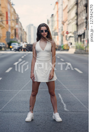 Portrait of young beautiful woman in short white dress walking on the street, summer outdoors. Portrait of young beautiful woman in short white dress walking on the street, summer outdoors. 127842470