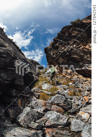 Backpacking woman climbing up on steep cliff edge at high altitude mountains top 127842543