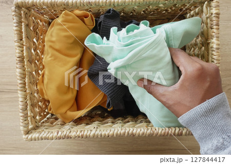 Organizing and arranging clothes in a woven basket for a neat look 127844417