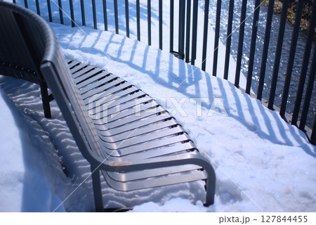 雪に覆われた川沿いのベンチと冬の川面 127844455