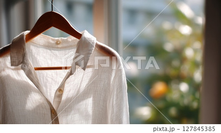 White Shirt Hanging on Wooden Hanger Near Window 127845385