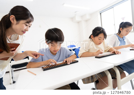 そろばん教室で学ぶ小学生と先生 127846780