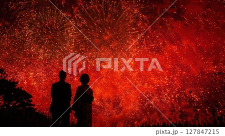 赤く染まる夜空に打ち上がる花火と見上げる二人のシルエット 127847215