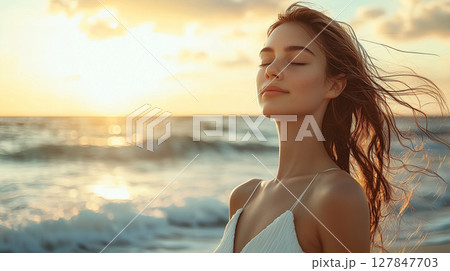 夕日に照らされた海辺で目を閉じて風を感じる美しい女性 127847703