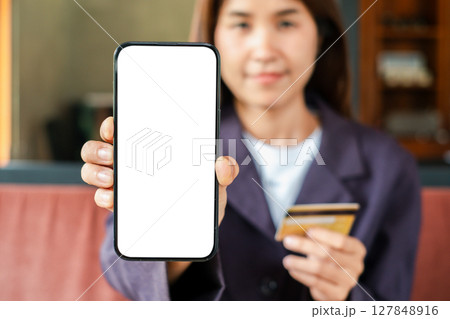 Close-up of a woman displaying a smartphone with a blank screen and holding a credit card, ideal for online shopping themes. Close-up of a woman displaying a smartphone with a blank screen and holding a credit card, ideal for online shopping themes. 127848916