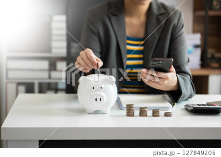 Business woman hand putting money coin into piggy bank with step of growing stack coins for saving money with virtual icon Business woman hand putting money coin into piggy bank with step of growing stack coins for saving money with virtual icon 127849205