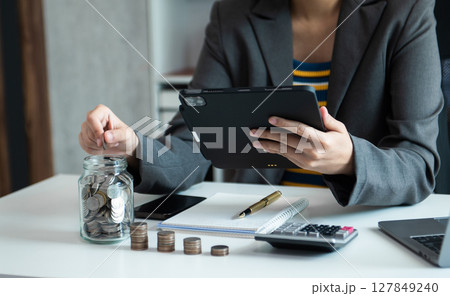 saving money with hand putting coins in jug glass and calculator to calculate budget concept finance and accounting saving money with hand putting coins in jug glass and calculator to calculate budget concept finance and accounting 127849240