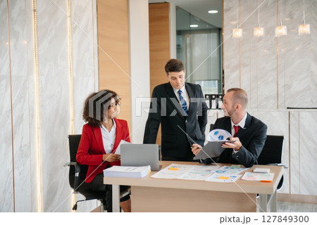 Group of young business people discussing business plan at modern startup in creative business discussing work modern office building Group of young business people discussing business plan at modern startup in creative business discussing work modern office building 127849300