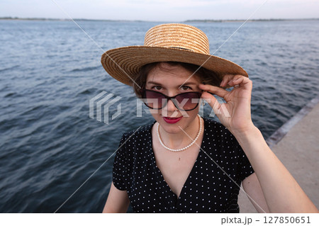 Close-up of stylish woman lifting sunglasses with gentle smile. Close-up of stylish woman lifting sunglasses with gentle smile. 127850651