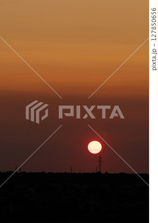Bright sun sets above horizon with warm orange glow 127850656