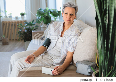 Senior woman checking blood pressure at home, looking concerned about health condition 127851006