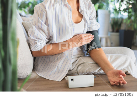 Senior woman measuring blood pressure with electronic monitor at home, health check concept 127851008