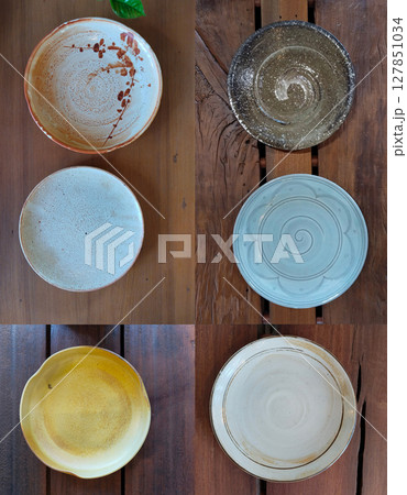A top-down shot of several unique ceramic plates in different colors and designs, set on a rich wooden table, highlighting the artistry of handmade tableware. A top-down shot of several unique ceramic plates in different colors and designs, set on a rich wooden table, highlighting the artistry of handmade tableware. 127851034