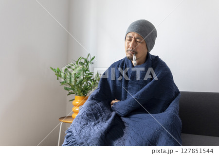 Asian man sick or ill and coughing by covering their mouth with napkin paper while sitting on the sofa at home. Asian man sick or ill and coughing by covering their mouth with napkin paper while sitting on the sofa at home. 127851544