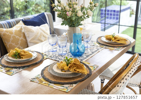 Plate setting with yellow handkerchief on wood table with artificial flowers on the dining table.  127851657