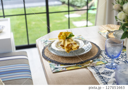 Plate setting with yellow handkerchief on wood table with artificial flowers on the dining table.  Plate setting with yellow handkerchief on wood table with artificial flowers on the dining table.  127851663