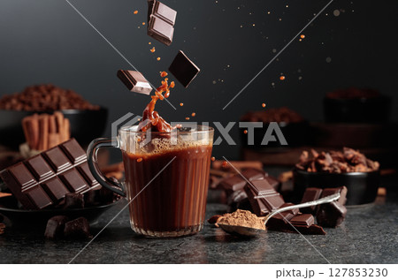 Pieces of dark chocolate fall into a mug of cocoa drink. 127853230