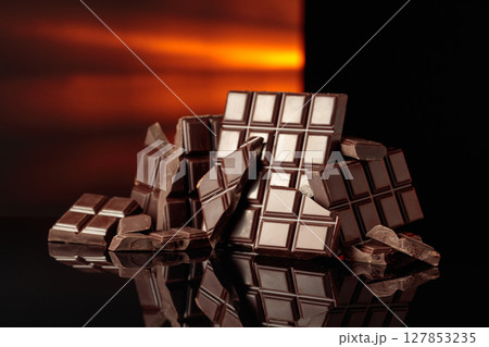 Broken bitter chocolate bars on a black glossy background. Broken bitter chocolate bars on a black glossy background. 127853235