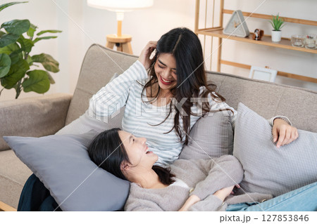 Young smiling gay couple in casual wear spend time together while sitting on couch in cozy living room 127853846