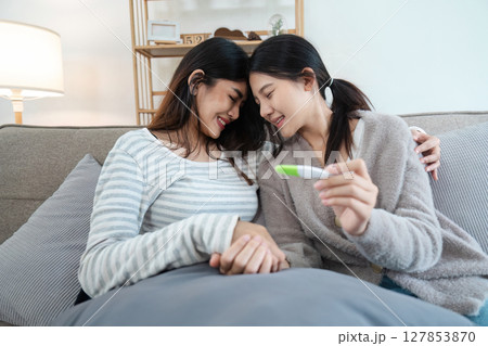 Two happy gay lesbian lgbt women couple sitting on sofa celebrating positive pregnancy test. lgbtq concept Two happy gay lesbian lgbt women couple sitting on sofa celebrating positive pregnancy test. lgbtq concept 127853870