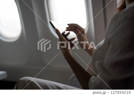 Asian business woman on aeroplane using smartphone Asian business woman on aeroplane using smartphone 127854219