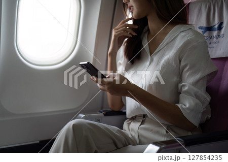 Asian business woman on aeroplane using smartphone Asian business woman on aeroplane using smartphone 127854235