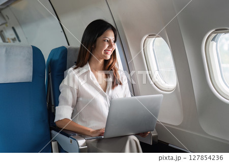 businesswoman flying and working in an airplane in first class, sitting inside an airplane using laptop businesswoman flying and working in an airplane in first class, sitting inside an airplane using laptop 127854236