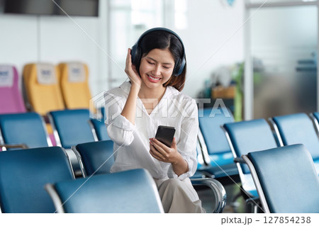 Woman listening to music on headphones in airport lounge, use smartphone and earphones while waiting for her flight 127854238