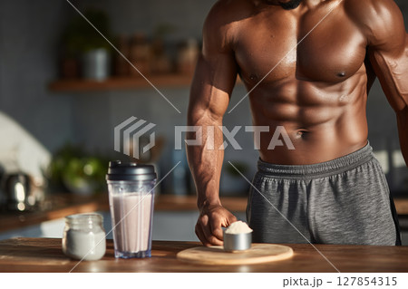 Muscular man preparing a protein shake in a bright kitchen 127854315