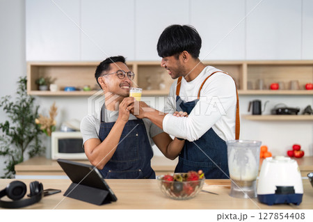 LGBT couple sharing a toast in the kitchen. Celebrating love with homemade drinks. LGBT couple sharing a toast in the kitchen. Celebrating love with homemade drinks. 127854408