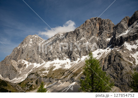 Dramatic Dachstein mountain peaks with lush green valley and clouds in Austria 127854752