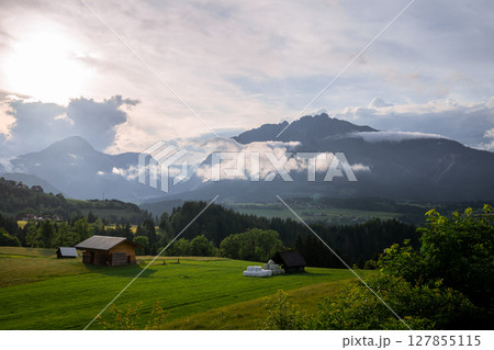 Peaceful alpine valley with wooden barns, green meadows and misty mountains at sunset in Austria 127855115