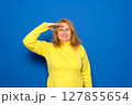 A smiling and proud Caucasian woman in her 40s saluting the camera in an act of honor and patriotism, showing respect. Isolated on a blue background 127855654