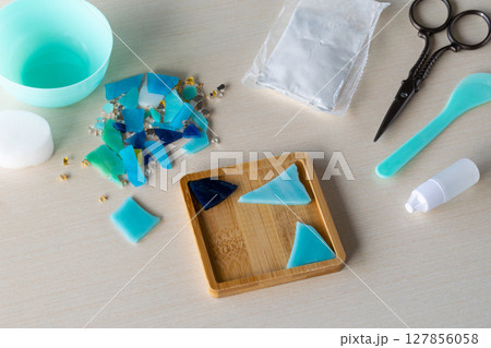 Colorful glass-like fragments prepared for DIY mosaic coaster in silicone mold with gypsum powder and craft tools on table before pouring process begins, step 1 Colorful glass-like fragments prepared for DIY mosaic coaster in silicone mold with gypsum powder and craft tools on table before pouring process begins, step 1 127856058